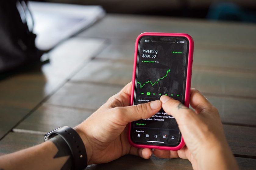 Mãos segurando um celular com o aplicativo de controle financeiro aberto, mostrando saldo e gráfico de evolução