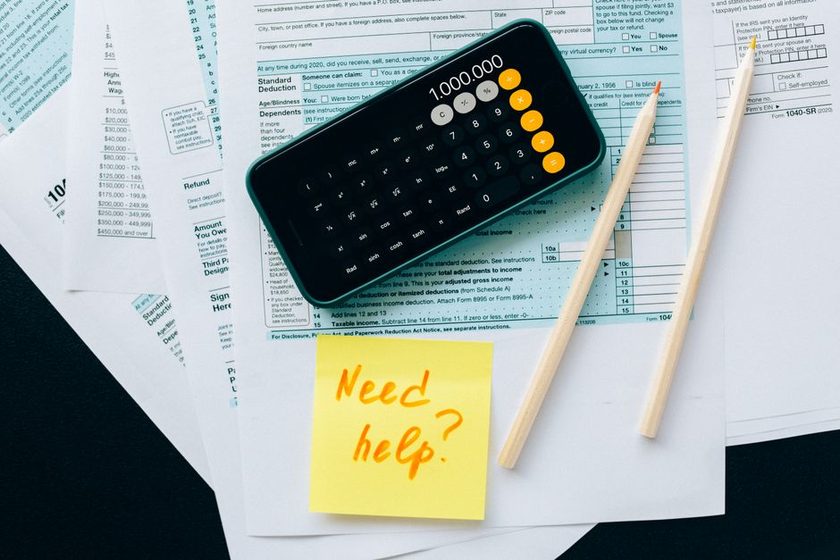 Formulários de declaração de imposto de renda sobre a mesa, com calculadora, lápis e um post-it de dúvida
